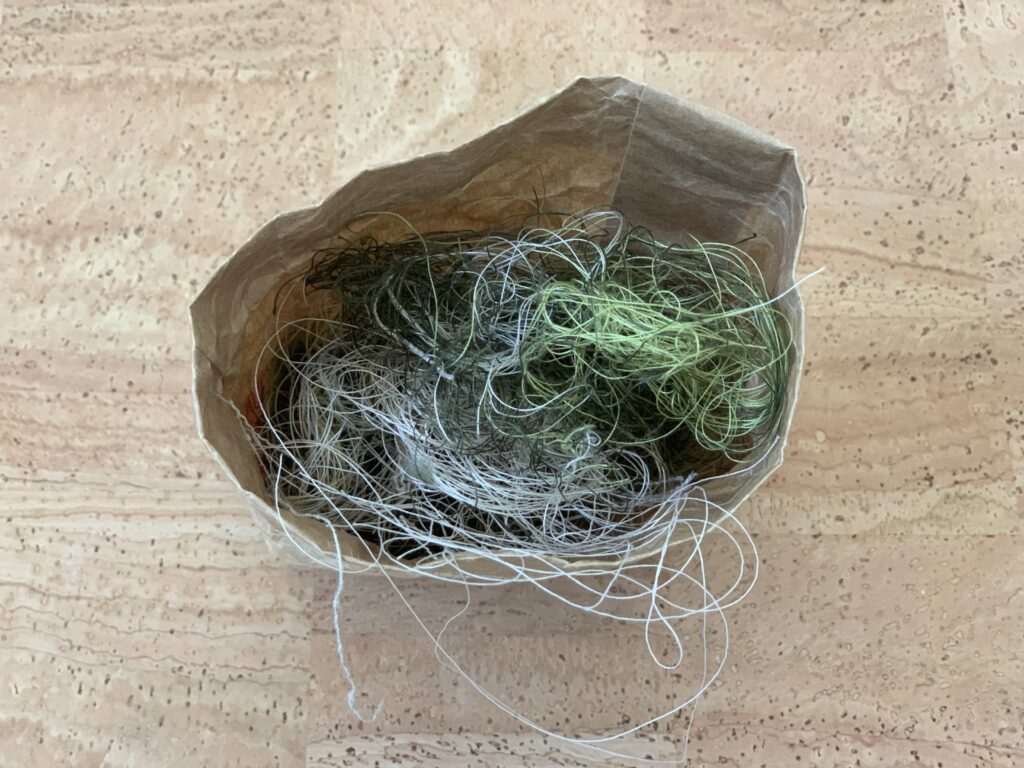 eine Tüte auf einem Korkhintergrund aus der Fadenreste herausschauen